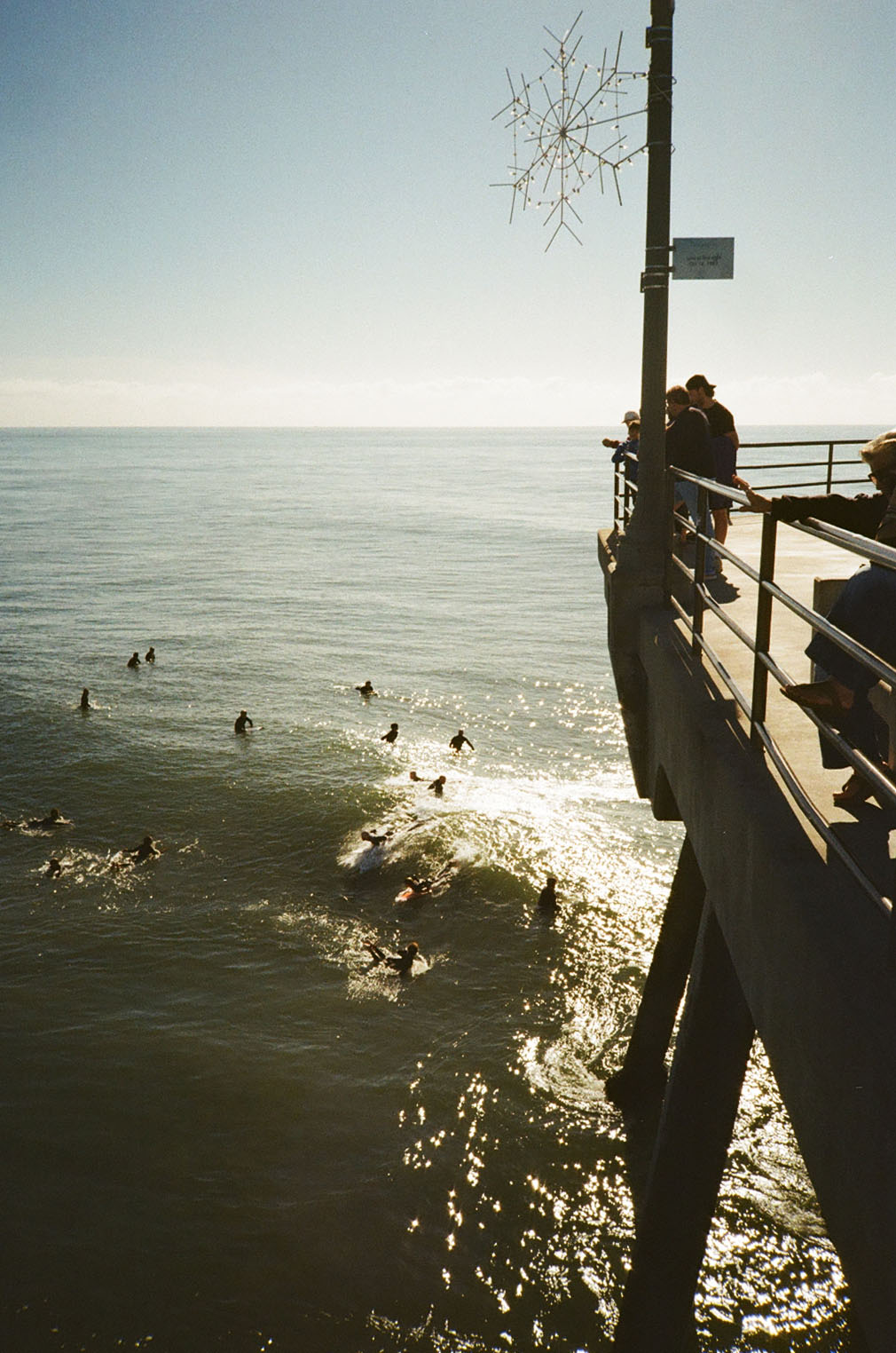 Surfers waiting for a wave with onlookers on the pier above